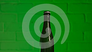 The neck of a green beer bottle closed with a lid with a brick green wall