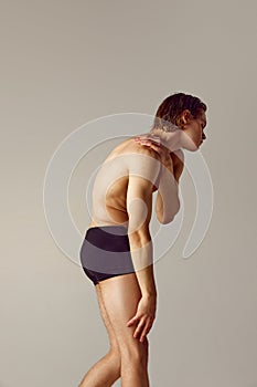 Neck and hand pains. Shirtless young man with fit body standing in underwear against grey studio background