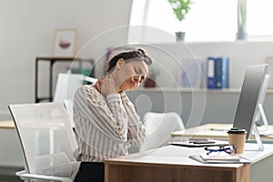 Neck pain. Exhausted young female entrepreneur massaging aching neck, suffering from ache, sitting in office