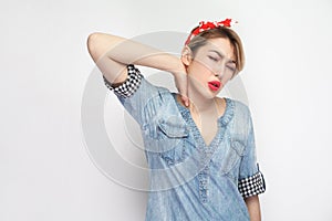 Neck pain. Portrait of sad young woman in casual blue denim shirt with makeup and red headband standing, closed eyes and holding