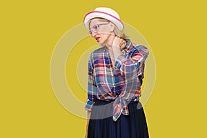Neck pain. Portrait of sick modern stylish mature woman in casual style with hat and eyeglasses standing and holding her painful
