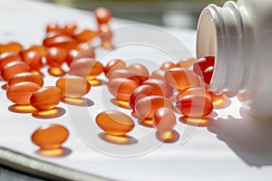 The neck of a white jar and orange pills and vitamins in random order on a table with papers.