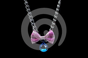 The Necklace for cats or pets made of silver chain with blue bell and pink and white bow on a completely black background