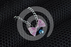 The Necklace for cats or pets made of silver chain with blue bell and pink and white bow on small black net background