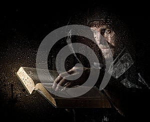 Necromancer casts spells from thick ancient book, behind transparent glass covered by water drops on a dark background