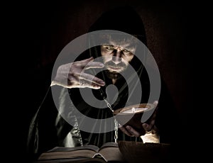 Necromancer casts spells from thick ancient book by candlelight on a dark background