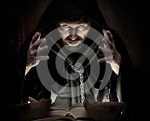 Necromancer casts spells from thick ancient book by candlelight on a dark background