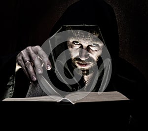 Necromancer casts spells from thick ancient book by candlelight on a dark background