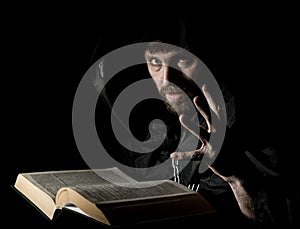 Necromancer casts spells from thick ancient book by candlelight on a dark background