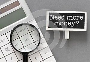 NEED MORE MONEY? words on a small chalkboard next to a calculator and magnifier
