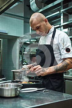 Need more spices. Vertical photo of restaurant chef with several tattoos adding a special spice to fresh cooked pasta