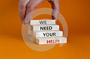 We need your help symbol. Wooden blocks with concept words `We need your help`. Businessman hand. Beautiful orange background.