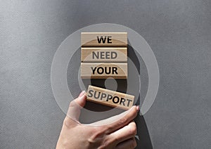We need your support symbol. Wooden blocks with words We need your support. Beautiful grey background. Businessman hand. Business
