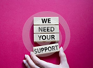 We need your support symbol. Wooden blocks with words We need your support. Beautiful red background. Businessman hand. Business