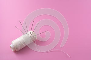 needle pierced or stick on white thread, symbol of garment industry, textile or fabric isolated pink background