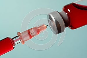 Needle pierces the cap of medical vial with red liquid
