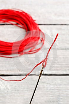 Needle with red thread, focus on the eye of a needle, on wooden background