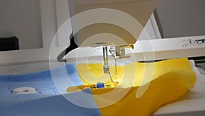 The needle of the sewing machine for embroidery makes an ornament on a piece of blue and yellow fabric. Special sewing