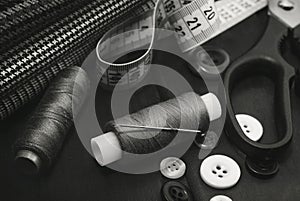 A needle with thread, buttons and scissors lie on a wooden background. Black and white photo