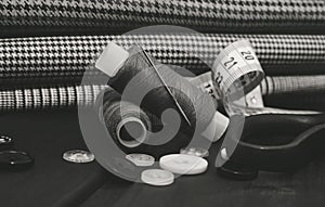 A needle with thread, buttons and scissors lie on a wooden background. Black and white photo