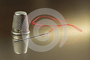 Needle, thread and red thimble