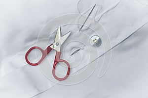 Needle thread scissors and button over white shirt