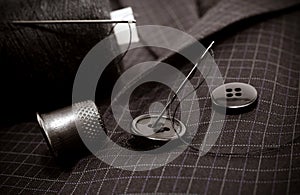 A needle and thread sews up a button on a plaid suit. Thimble. Textile