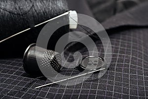 A needle and thread sews up a button on a plaid suit. Thimble. Textile