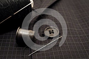 A needle and thread sews up a button on a plaid suit. Thimble. Textile