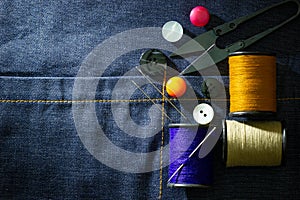 Needle and threads against plastic button and thread cutting scissors on jeans fabric.