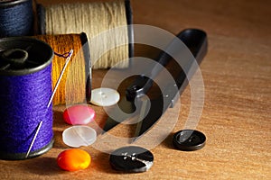 Needle and threads against plastic button and thread cutting scissors on wooden table.