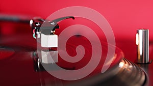 Needle of Vintage DJ Turntable Spinning Vinyl Record on red background Close Up