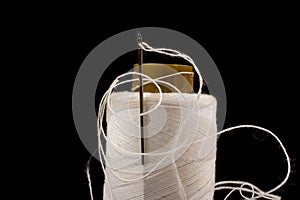 Needle and white cotton, tangled yarn on roll for sewing. Thread used in fabric and textile industry. Black background