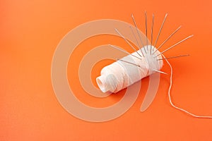 needle and white thread, sewing tools and garment symbol isolated on orange background