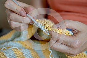 Needlework. Women`s hands close up crocheting children`s plaid. Crochet hook