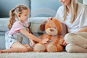 He needs a checkup. a little girl and her mother playing doctor with a teddybear at home.