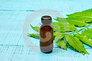 Neem oil in bottle and fresh green leaf on blue wooden background.