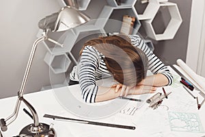 Negative emotions. Portrait of young fashionable female freelance architect lying on hands at table, being tired after