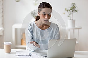 Negatively shocked millennial mixed race woman looking at computer screen.