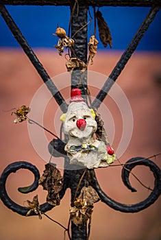 Neglected clown toy on fence with decaying flowers