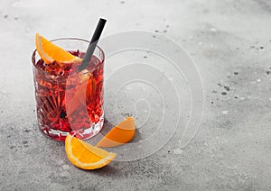 Negroni cocktail in crystal glass with orange slice and black straw on light background