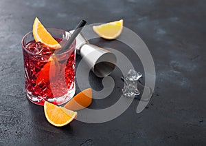 Negroni cocktail in crystal glass with orange slice and fresh raw oranges with jigger on black background