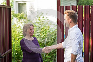 Neighbors discuss the news, standing at the fence. An elderly woman talking with a young man