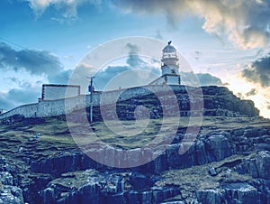 The Neist Point lighthouse on the end of world. Foamy sea strikes against the cliff.