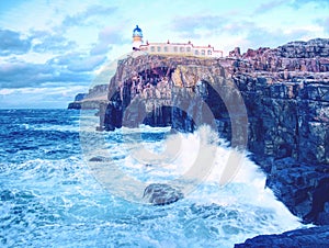 The Neist Point lighthouse on the end of world. Foamy sea strikes against the cliff.