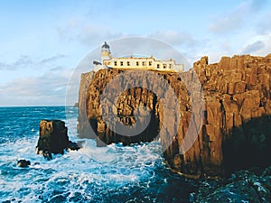 Neist Point lighthouse on rocky cliff above wavy sea. Blue evening sea and sharp cliffs,