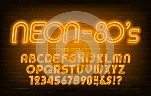 Neon alphabet font. Yellow neon light letters and numbers in 80s style. Brick wall background.