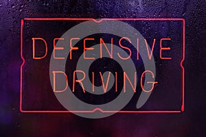 Vintage Neon Defensive Driving Sign in Rainy Window photo