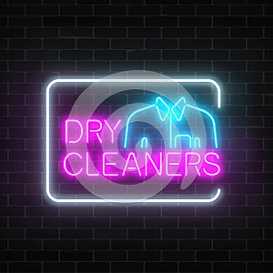 Neon dry cleaners glowing sign with shirt in rectangle frame on a dark brick wall background.