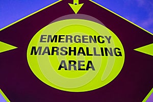 A neon emergency marshalling area sign with arrows